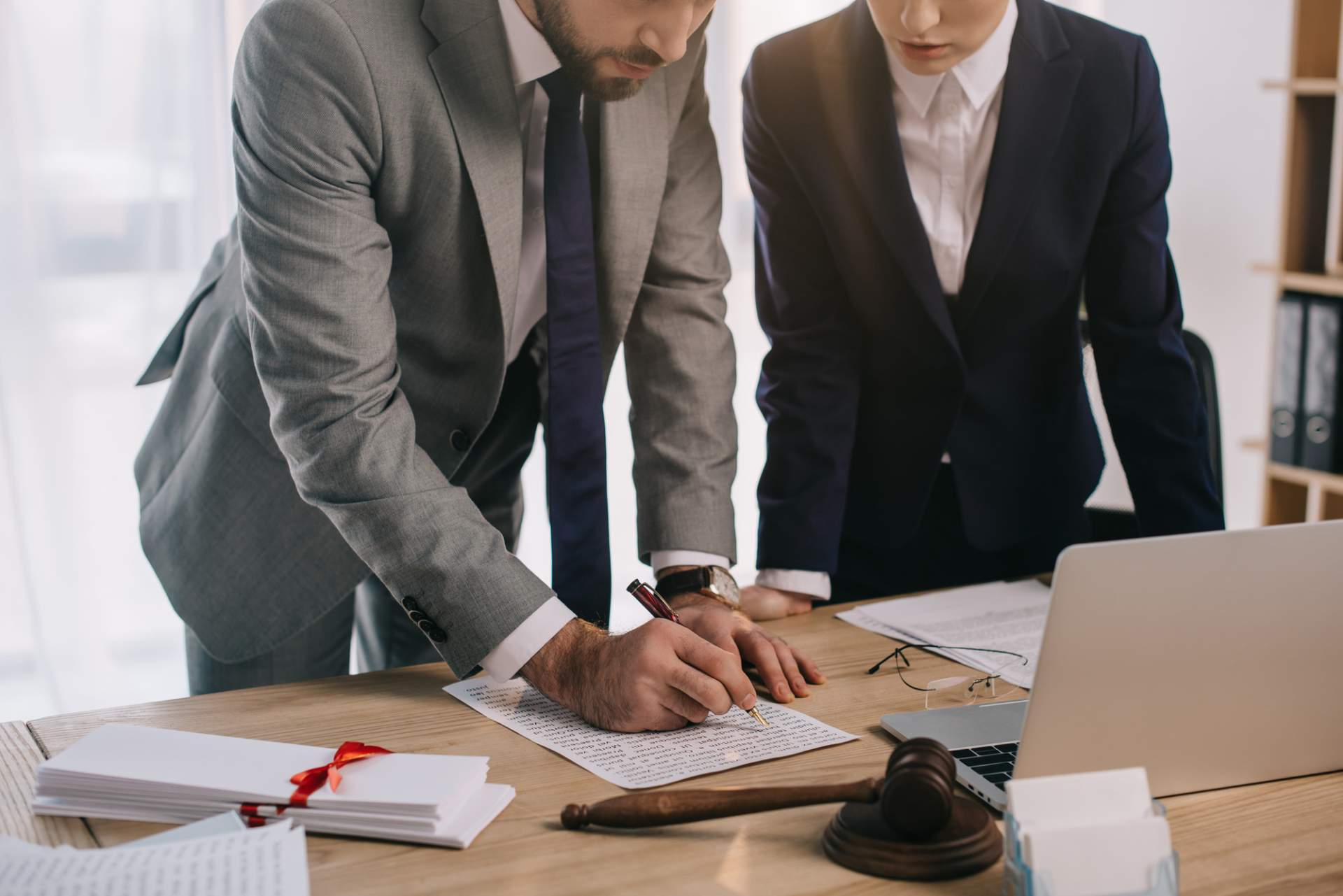 Attorneys in suits leaning over a desk signing forms